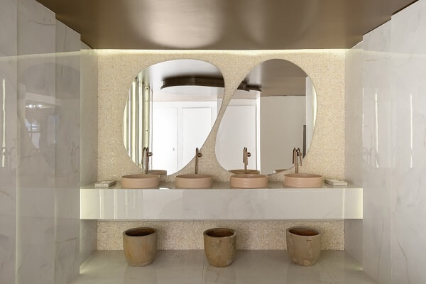 Banheiro cor areia e rose com espelhos em formato orgânico