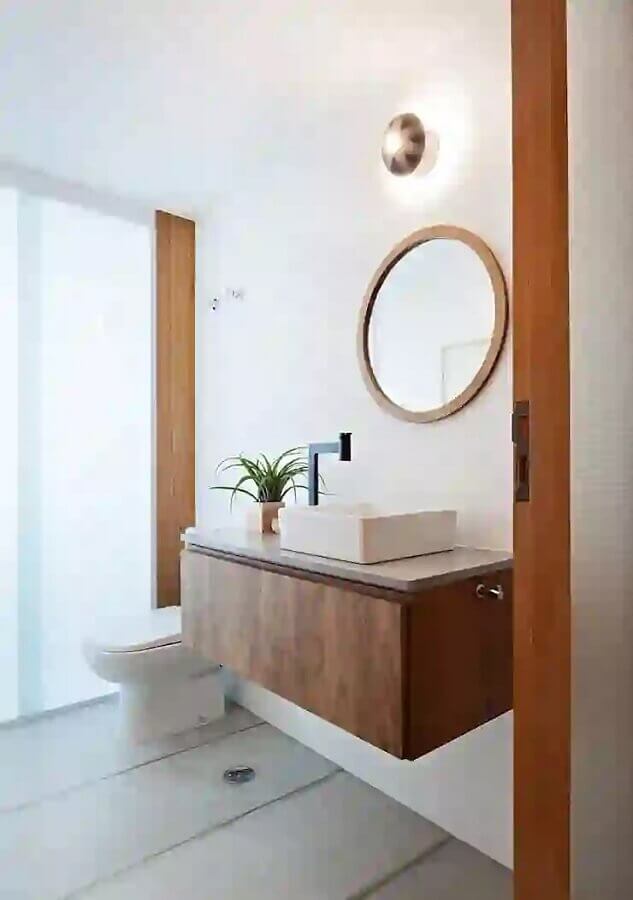 Banheiro minimalista decorado com gabinete suspenso e espelho redondo com moldura de madeira