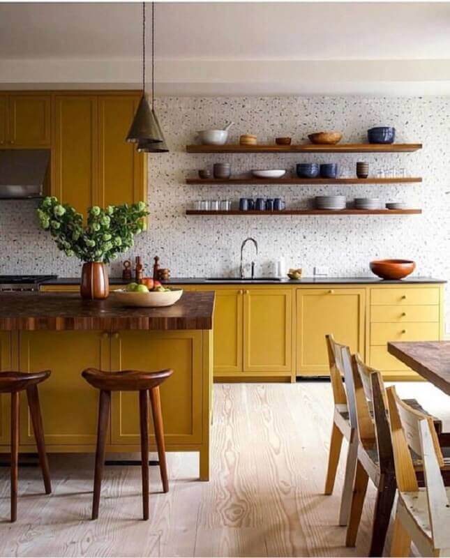 Cozinha com prateleira suspensa decorada com armários e ilha amarela
