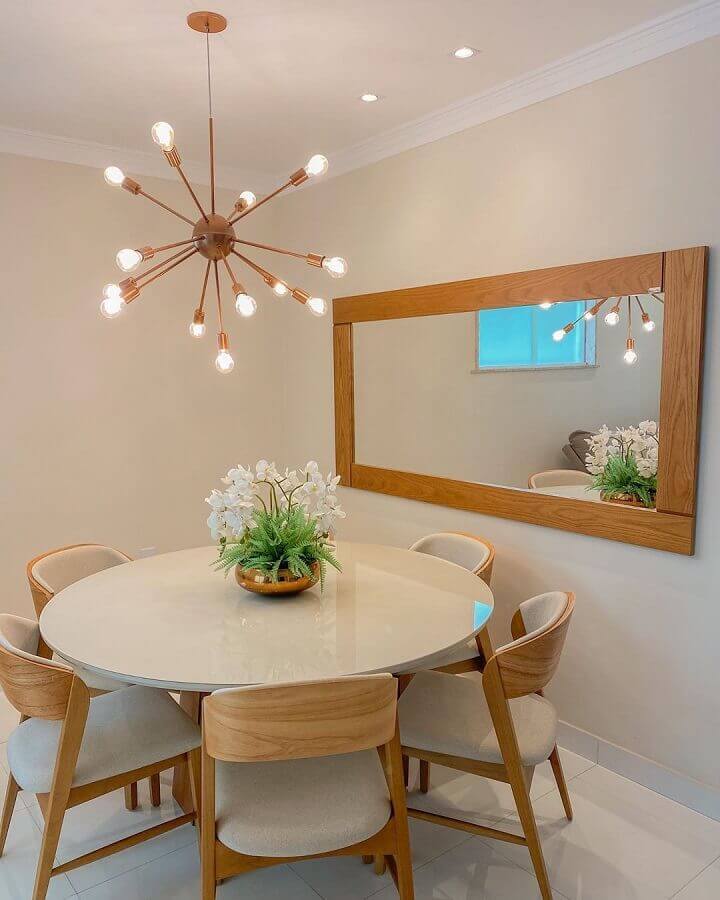 Sala de jantar decorada com mesa redonda e espelho com moldura de madeira 