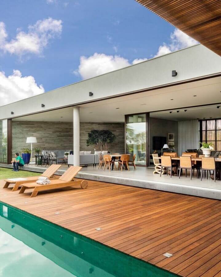 Casa grande com conceito aberto decorada com espreguiçadeira de madeira para piscina