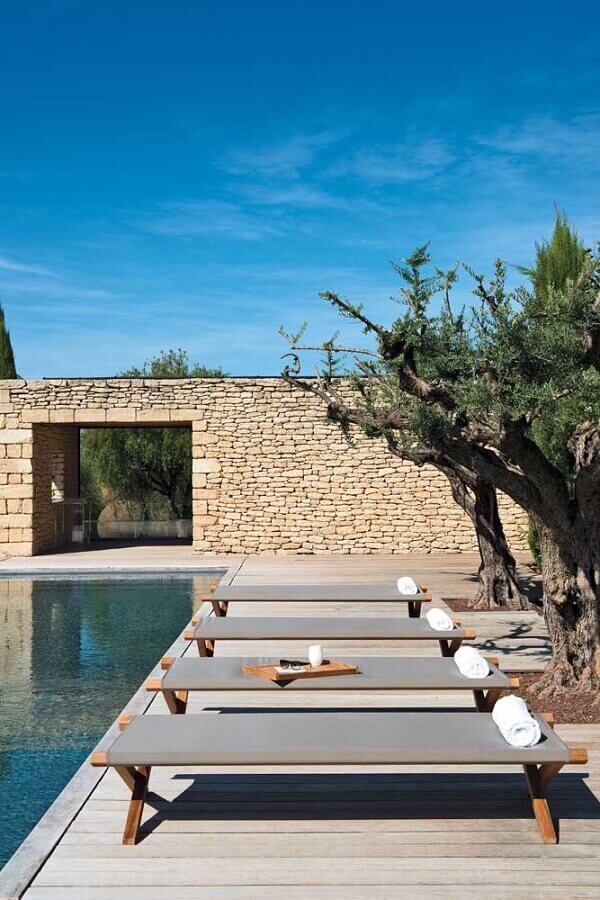 Área externa com cadeira espreguiçadeira de piscina minimalista e parede rústica